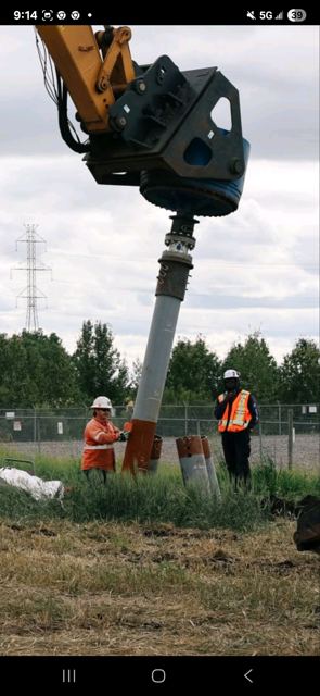 Excavator-mounted torque head installing a helical screw pile on a transmission alignment