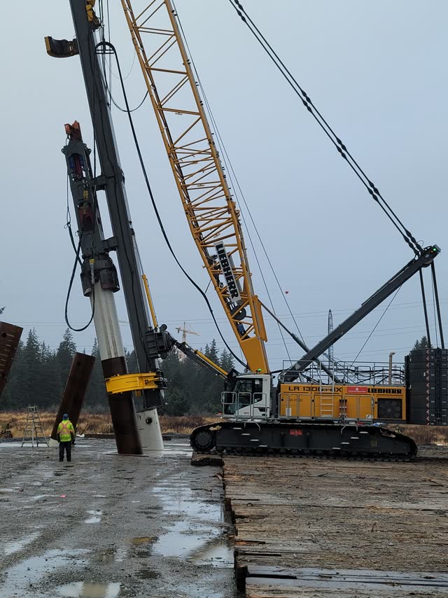 Crane with pile leads driving over water at a crossing
