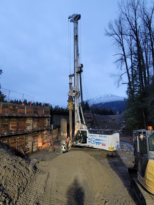 Cast-in-place shaft drilling beneath a rail bridge behind a shored excavation