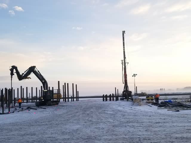 Pile rigs silhouetted on a frozen construction pad at dusk